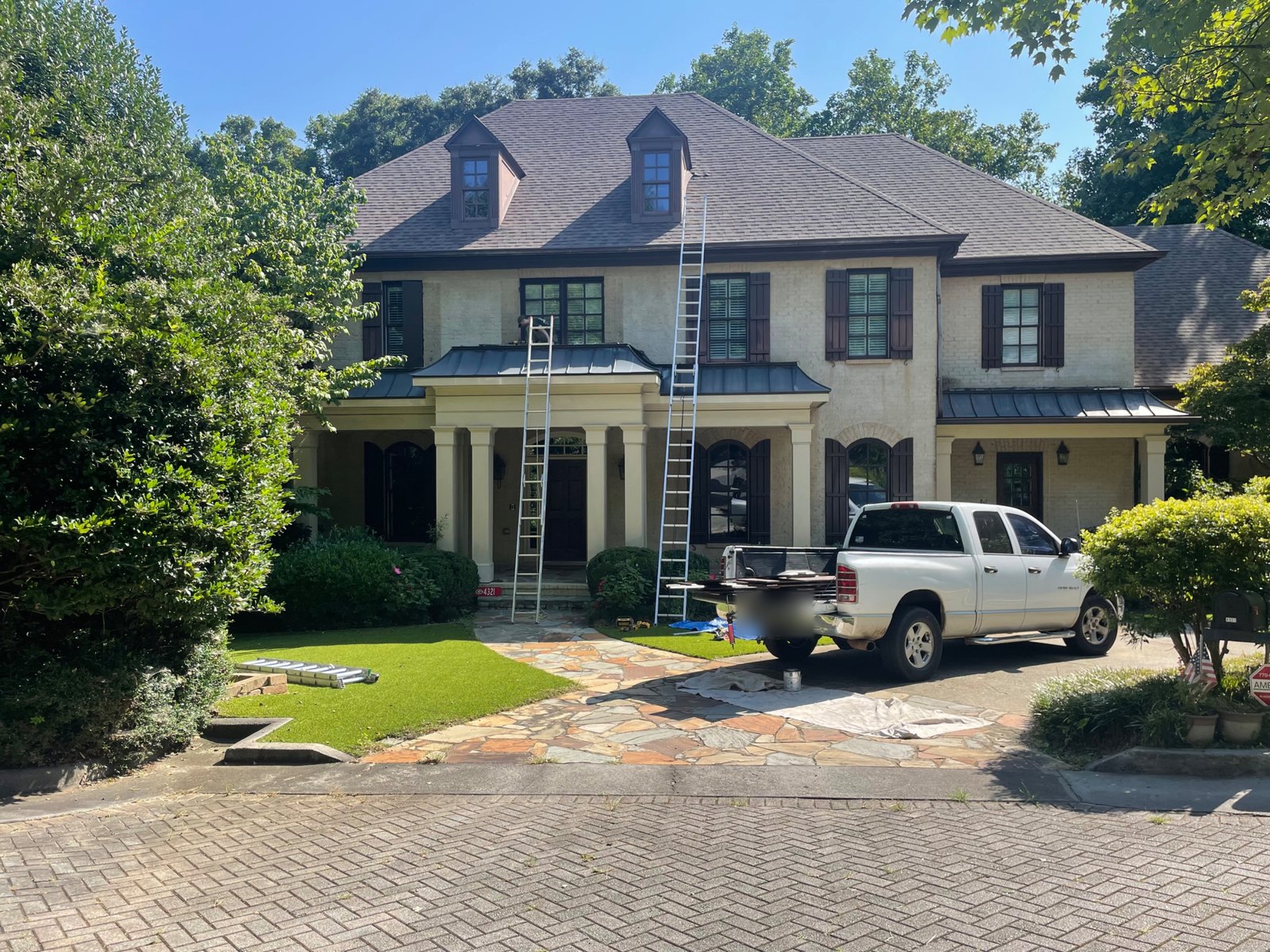 Ladders against a two-story brick house with new dark exterior shutters, a pickup truck in the driveway